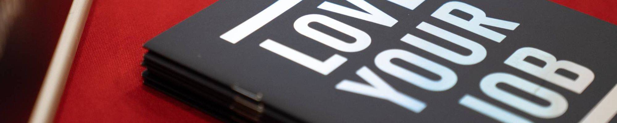 A black and white book saying "Love your job" on a red table cloth